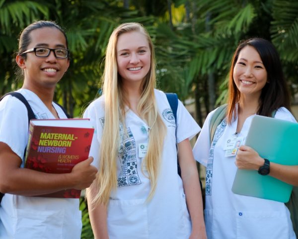 three nursing students pose for photo with study materials